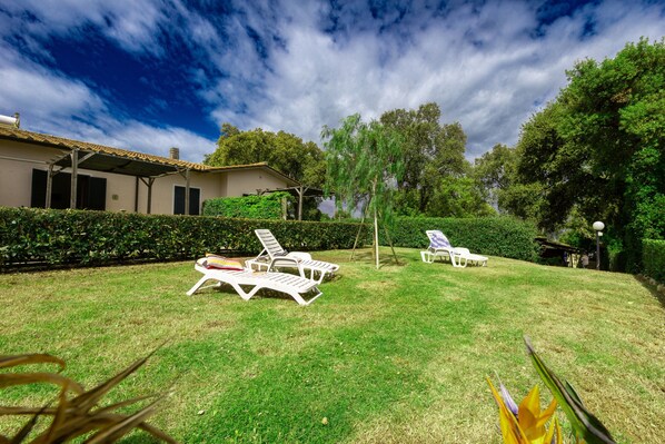 A backyard with white lounge chairs, a covered patio, and a house with a tiled roof.