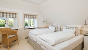 Een slaapkamer met twee bedden, een bureau, een stoel en een raam met gordijnen.