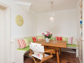 A dining area with a wooden table, a bench with colorful cushions, a clock, and a chandelier.