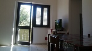 Een kamer met een eettafel, stoelen, een televisie en een raam met jaloezieën.
