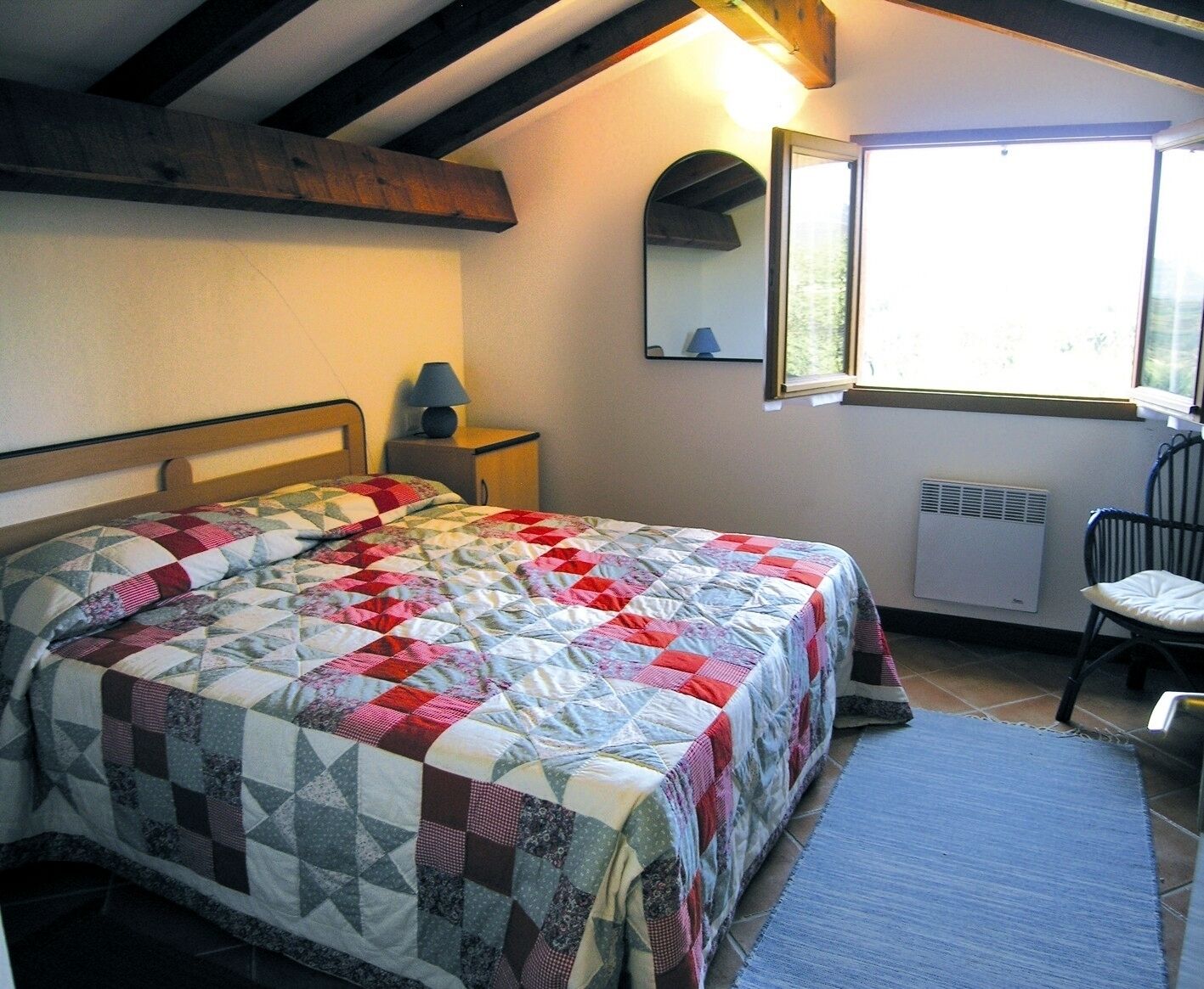 A bedroom with a bed, a nightstand, a chair, a window, and a radiator.