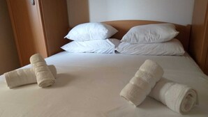 En pænt redt seng med hvide sengetøj og puder, samt to sammenrullet håndklæder placeret på sengen.