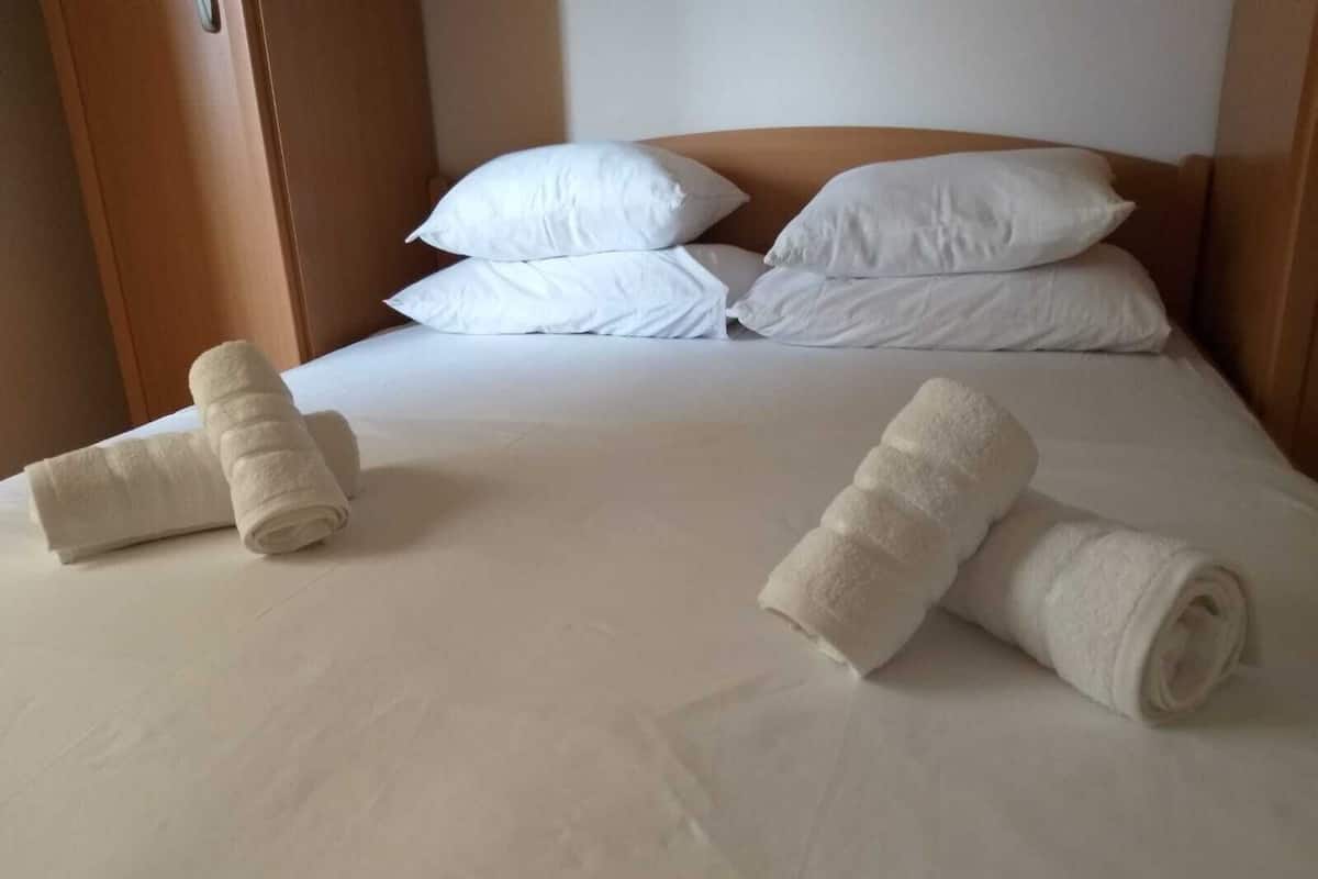 Una cama bien hecha con sábanas y almohadas blancas, y dos toallas enrolladas sobre la cama.