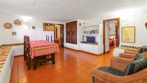 A room with a dining table, chairs, a sofa, a television, and a bookshelf. - Tranquil Apartment "Leccio" on the Beach with Terrace, Garden & Wi-Fi (San Teodoro)