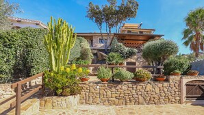A stone wall with potted plants, a wooden fence, and a building with a tiled roof. - Tranquil Apartment "Leccio" on the Beach with Terrace, Garden & Wi-Fi (San Teodoro)