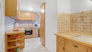 A kitchen with wooden cabinets, a microwave, and a sink. - Apartment "König" with Terrace, Wi-Fi, Garden & Mountain View (Berchtesgaden)