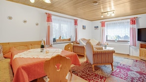 A cozy room with a bed, two chairs, a small table with a bottle, and a TV. - Apartment "König" with Terrace, Wi-Fi, Garden & Mountain View (Berchtesgaden)
