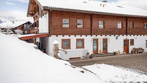 A wooden chalet with a snow-covered roof, multiple windows, and a front porch. - Apartment "König" with Terrace, Wi-Fi, Garden & Mountain View (Berchtesgaden)