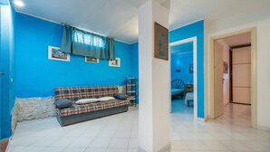 Una sala de estar con pared azul, un sofá de cuadros y un comedor visible a través de un arco.