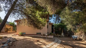 Un pequeño edificio con un sendero de piedra que conduce a una puerta, rodeado de árboles y un muro de piedra.