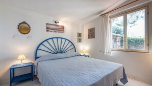 Un dormitorio con una cama, dos mesitas de noche con lámparas, un espejo en la pared y una ventana con cortinas.