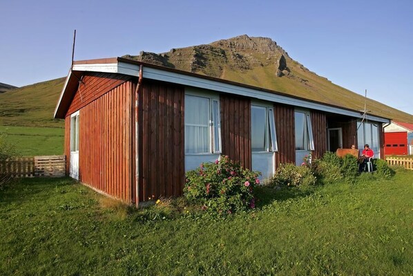 A wooden building with a sloped roof, large windows, and a person standing near the entrance.
