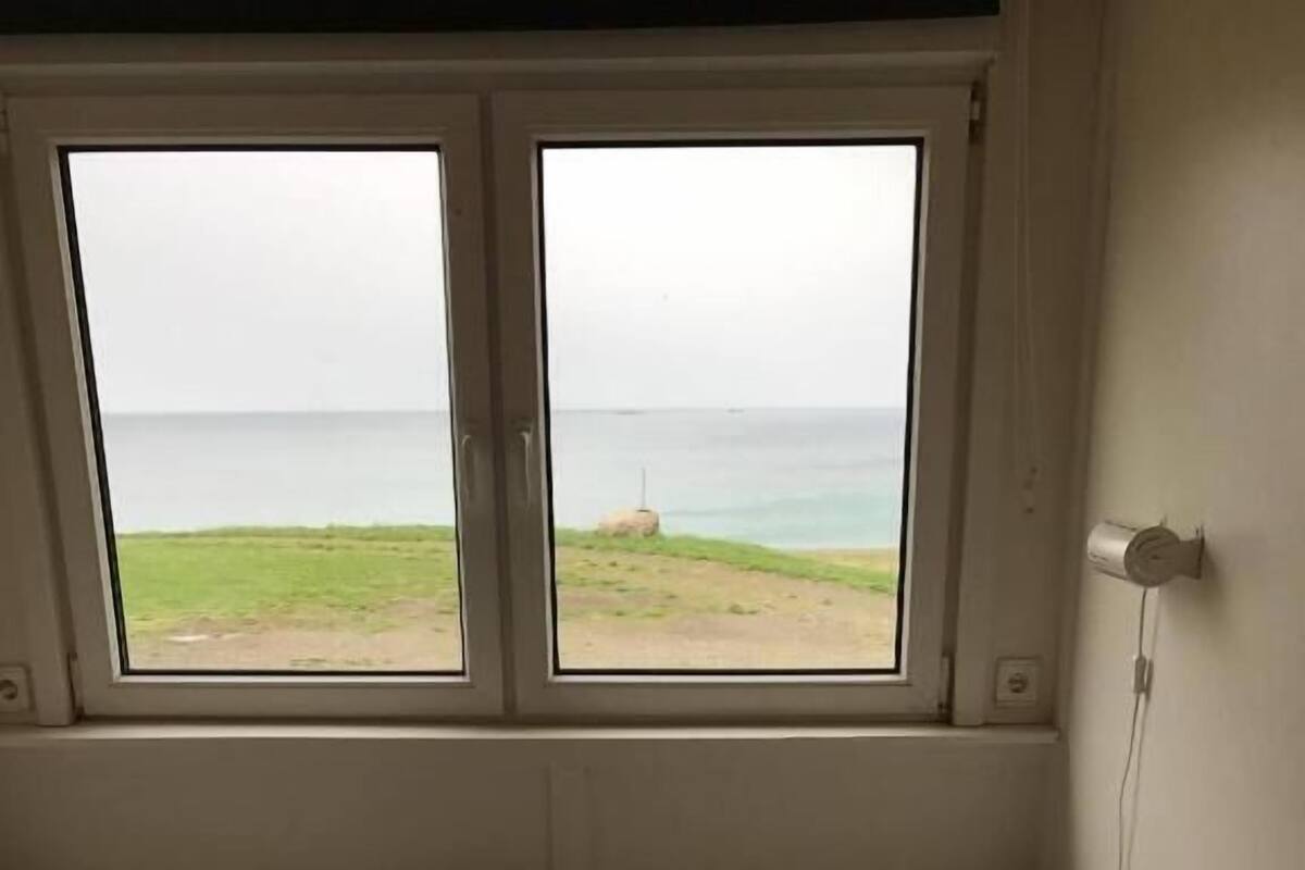 Una habitación con dos camas individuales, una ventana con vista al mar y un enchufe de pared.