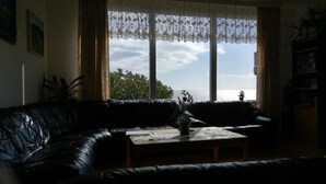 Un salon avec un canapé en cuir noir, une table basse en bois et une vue sur la mer grâce à de grandes fenêtres.