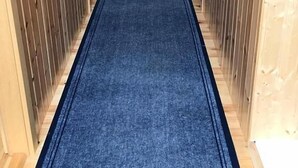 Un long couloir étroit aux murs en bois et recouvert d’un tapis bleu.