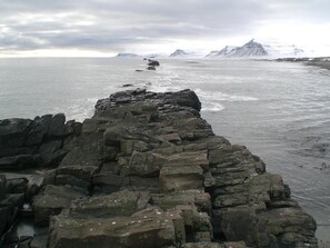 A rocky shoreline with a view of the sea and distant mountains.
