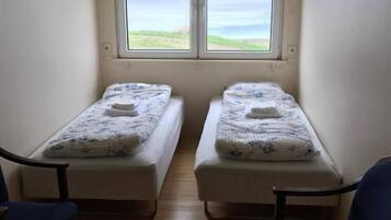 A small room with two single beds, a window with a view of the sea, and two blue chairs.