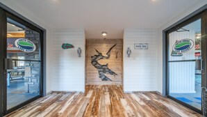 Un pavimento in legno con un mosaico centrale, due porte con insegne e un logo apposto sulle pareti.