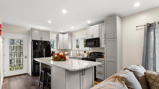 A modern kitchen with white cabinets, a granite countertop, a central island with a flower arrangement, a black refrigerator, a microwave, and a stove. - The Overlook at Orchard Hills -- Hilltop Retreat,  Near Acadia (Tremont)