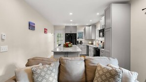 A modern kitchen with grey cabinets, a central island, and a dining area with a sofa and cushions. - The Overlook at Orchard Hills -- Hilltop Retreat,  Near Acadia (Tremont)