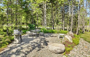 Relax in a serene outdoor setting with a patio area, table, and chairs surrounded by trees and shrubs, perfect for dining and outdoor activities.
