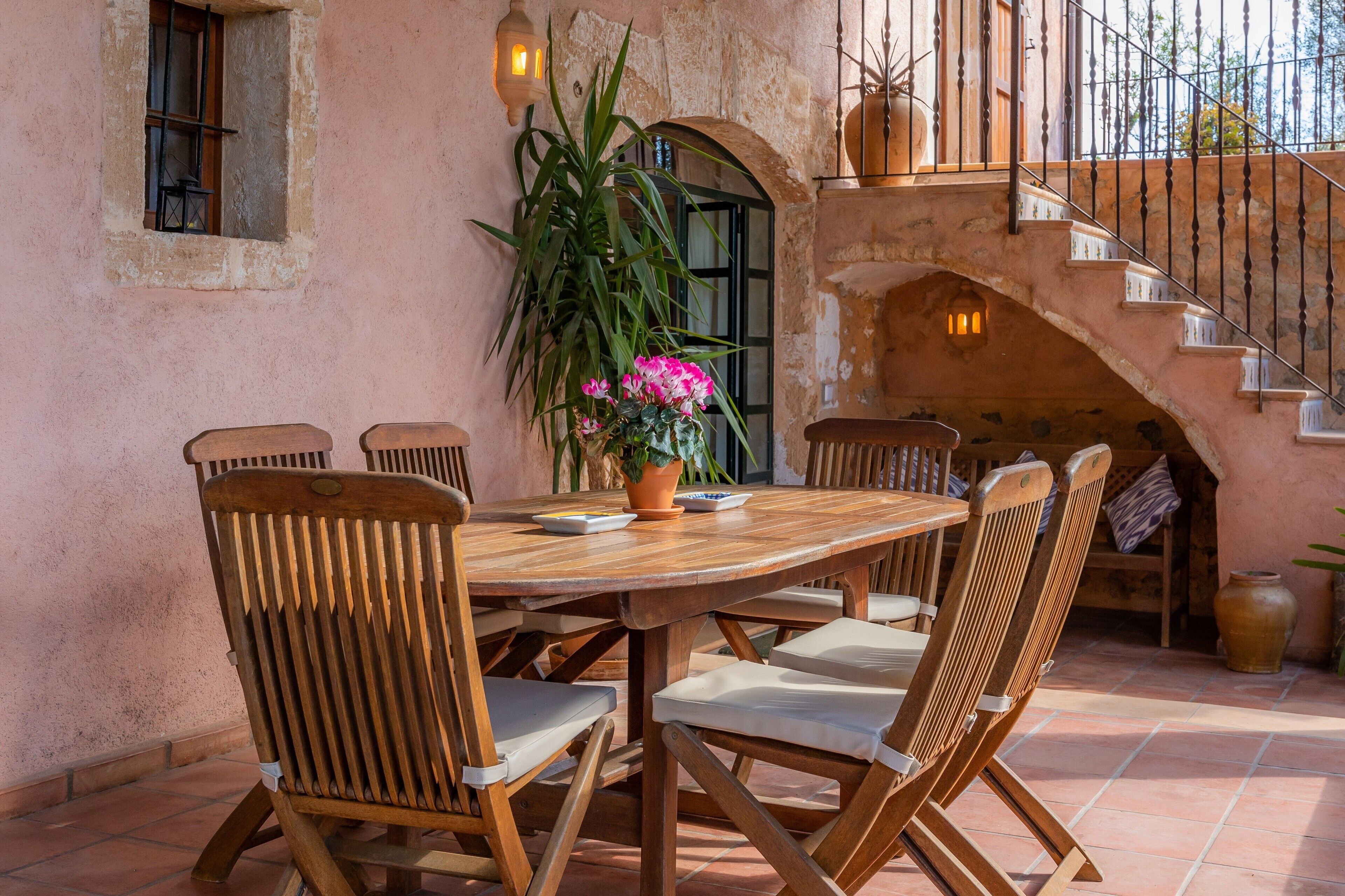 Una mesa de madera con sillas, una planta en maceta con flores y una escalera con barandilla.
