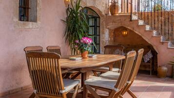 Una mesa de madera con sillas, una planta en maceta con flores y una escalera con barandilla.