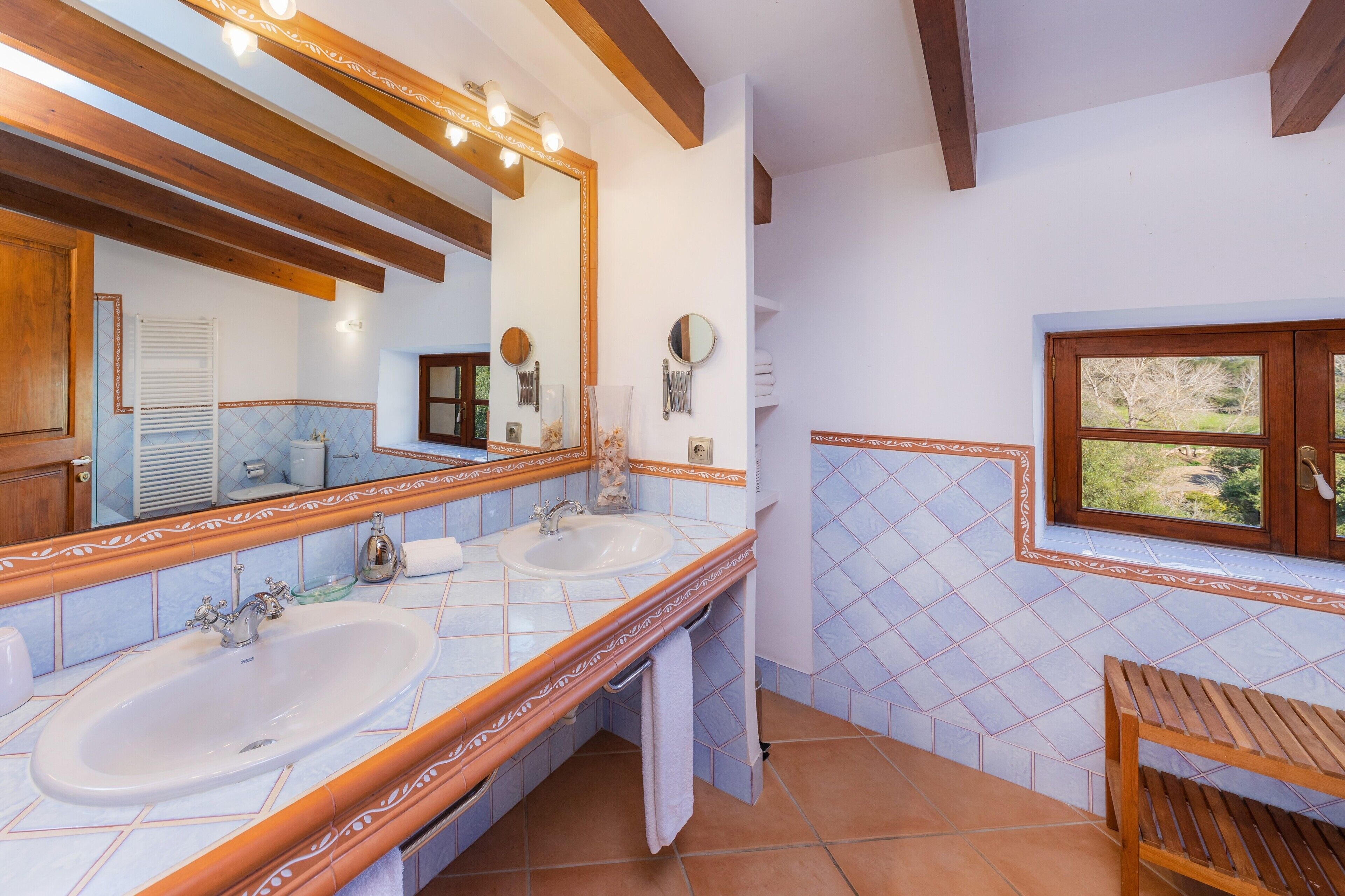 A bathroom with two sinks, a large mirror, wooden beams, and a window with a view.