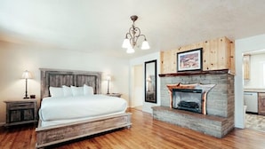 A bedroom with a large bed, a stone fireplace, wooden cabinets, and a chandelier. - Bryce Canyon Pines (Bryce Canyon)