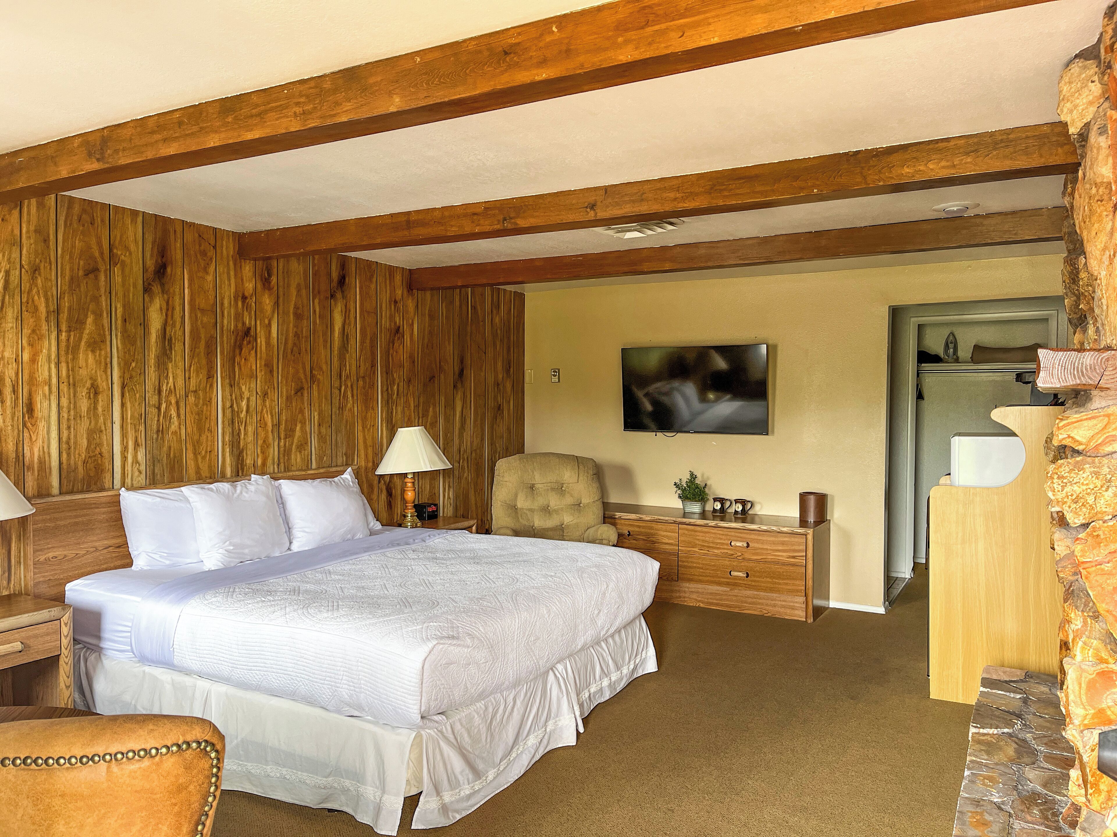 A bedroom with a bed, bedside table, lamp, chair, and a television on the wall.