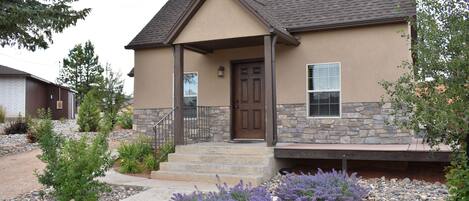 A two-story house with a stone facade, a front porch, and a well-maintained garden with purple flowers.