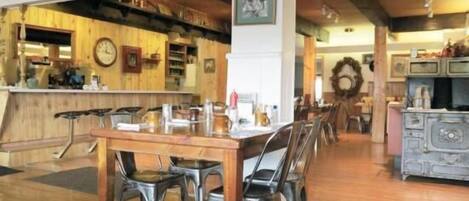 A dining area with a wooden table and chairs, a bar area with shelves and a clock, and a kitchen area with a sink and cabinets.