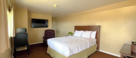 Una habitación de hotel con una cama grande, una silla, un televisor sobre un mueble bajo y una mesita.