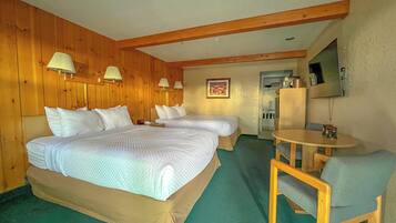 A hotel room with two beds, a small table, a chair, a television, and wooden walls.