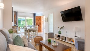 Een woonkamer met een bank, salontafel, televisie en een eethoek met stoelen en een tafel.