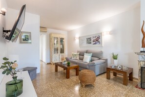 Ein modernes Wohnzimmer mit einer Couch, zwei Couchtischen, einem kleinen runden Hocker, einem an der Wand montierten Fernseher und einem Kamin.