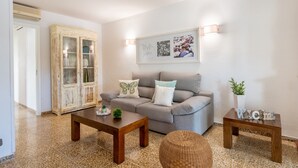 Een woonkamer met een bank, twee houten tafels, een rieten stoel, een kast met glazen deuren en een wandlamp.