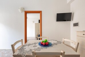 A dining area with a table set for two, a television mounted on the wall, and a door leading to another room.