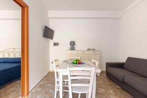 A compact living space with a dining table, white chairs, a sofa, and a TV mounted on the wall.