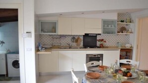 Una cucina compatta con mobili bianchi, forno a incasso e zona pranzo con tavolo apparecchiato per due persone.