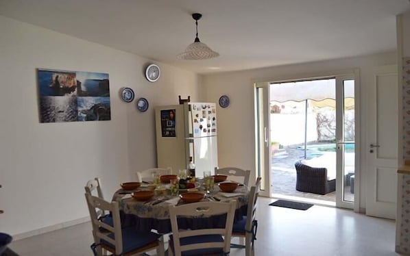 A dining area with a table set for four, a refrigerator, and a view of the outdoors.