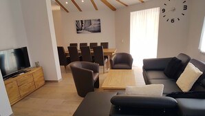 Una sala de estar moderna con un televisor de pantalla plana, un sofá, una mesa de centro y un comedor con sillas y una mesa.