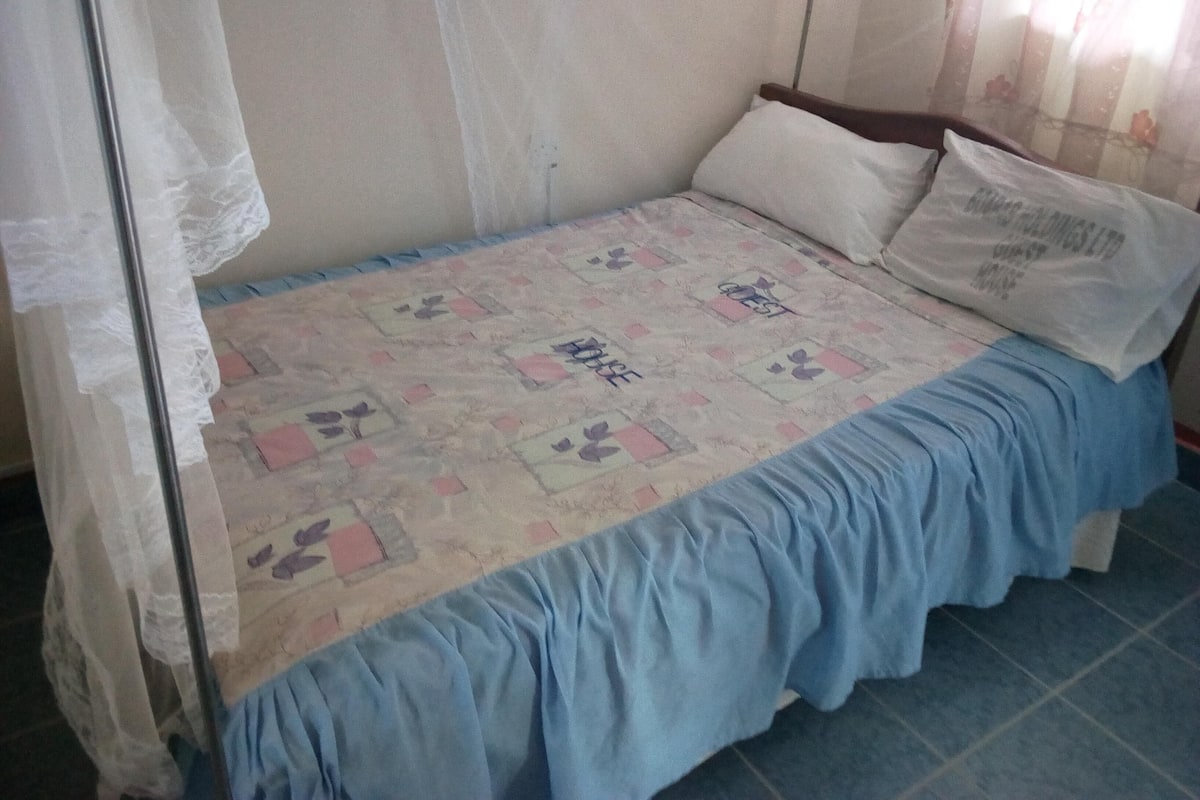 A single bed with a patterned bedspread, a blue skirted bed skirt, and a white pillow.