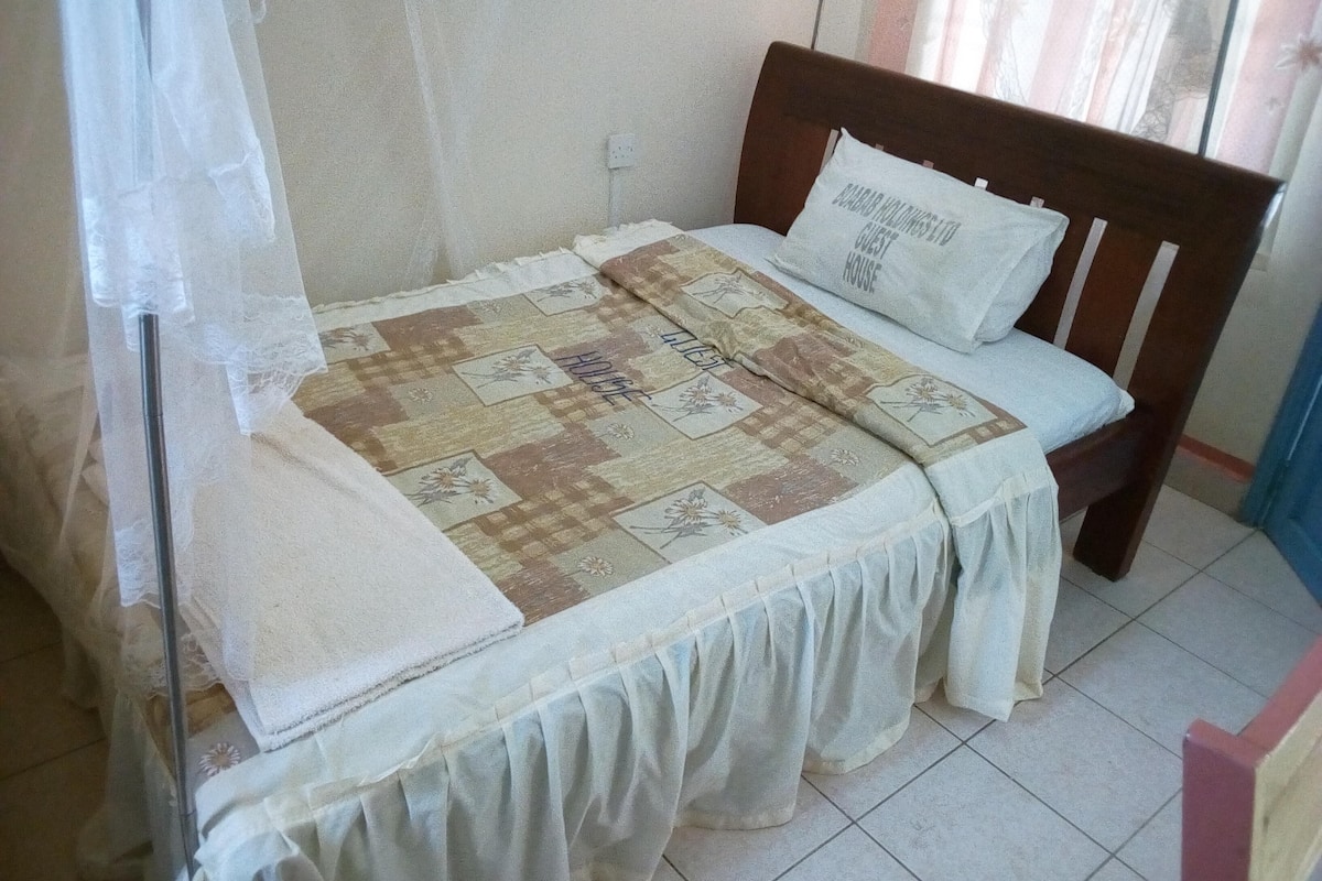 A single bed with a wooden headboard, a quilt with floral patterns, and a pillow with text.