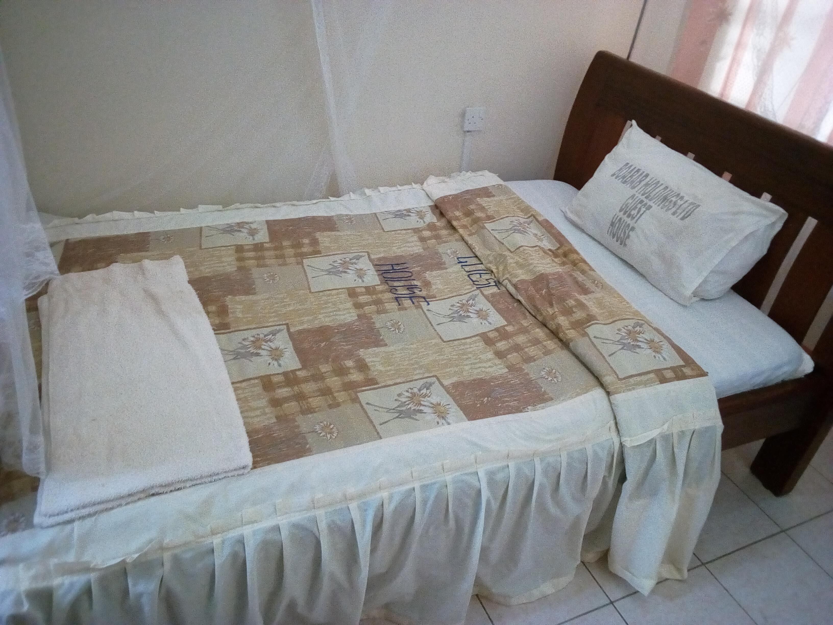 Una cama pequeña con colcha y almohada, una mesita de noche y un enchufe de pared.
