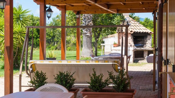 Un espace extérieur abrité, aménagé avec des sièges, d’où l’on peut admirer un bâtiment en pierre et un barbecue.