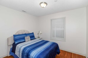 A bedroom with a bed, a nightstand, a lamp, and a window with blinds.