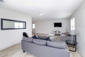 A modern living room with a grey sofa, a flat-screen TV mounted on the wall, and a small table with a lamp.