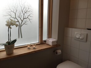 A bathroom with a window, a toilet, a towel rack, and a plant on the windowsill.