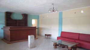 A room with a wooden reception desk, a red sofa, a glass-top coffee table, and a tiled floor. - Eden Garden Hotel (Wote)